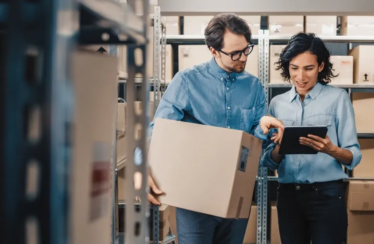 Two people checking box inventory on a tablet in a stockroom